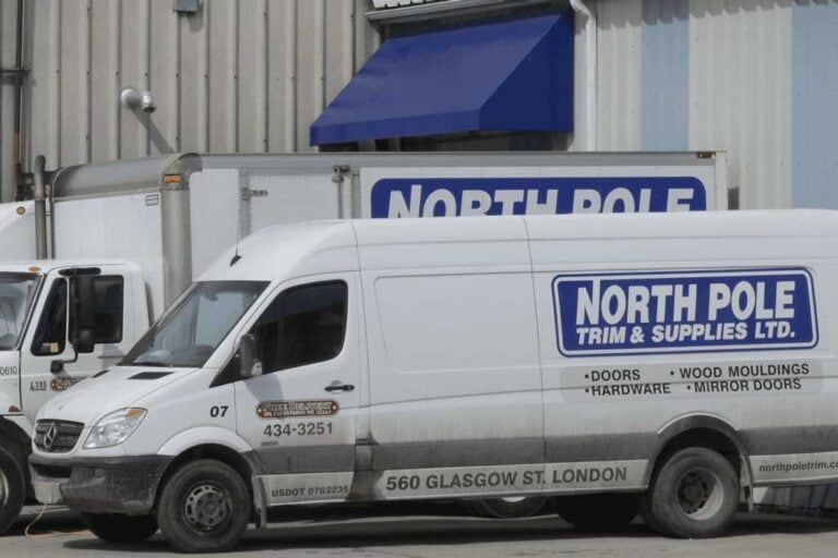 A white van and a truck parked outside a building, both branded with North Pole Trim & Supplies Ltd, advertising high-quality trim, doors, hardware, wood mouldings, and mirror doors.