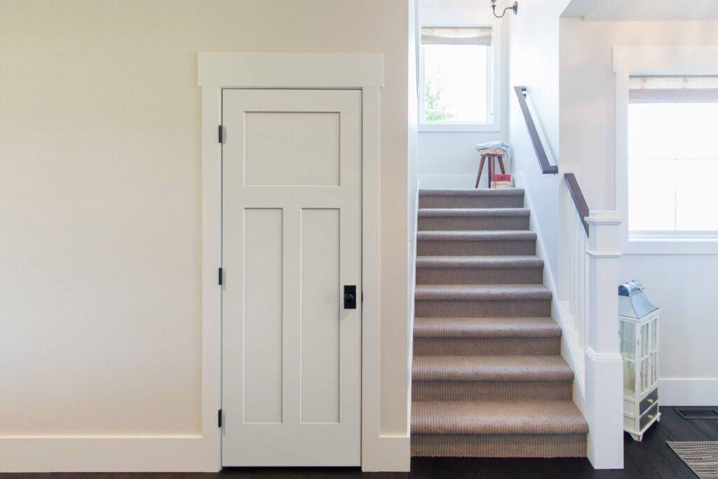 A sleek white interior door complements the carpeted staircase, illuminated by the window at the top.