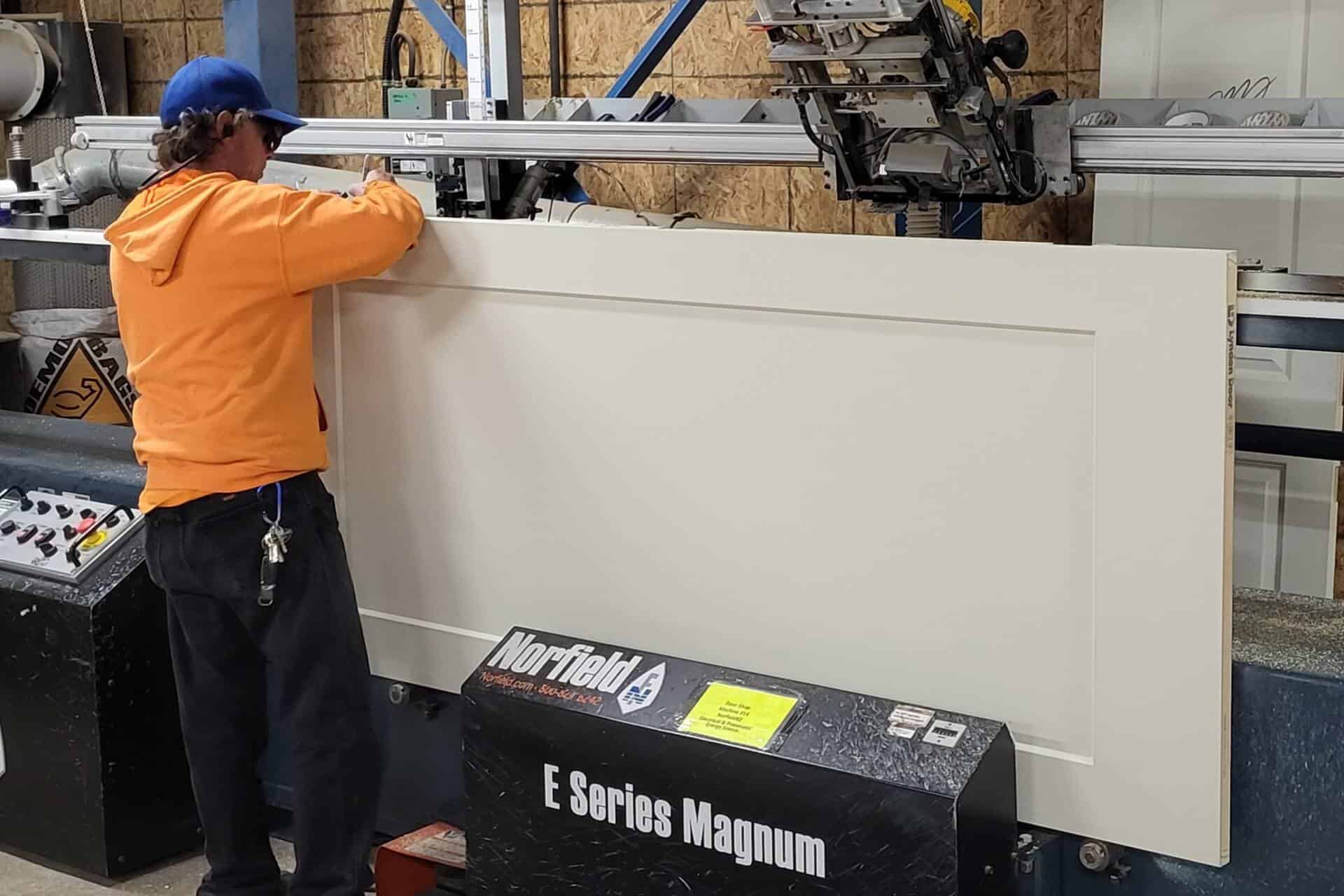 A worker in an orange hoodie is operating a Norfield E Series Magnum machine, skillfully installing a pre-hung door panel.