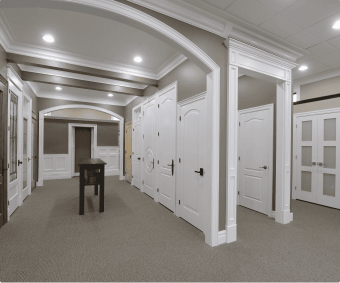 A spacious hallway with multiple white doors, recessed lighting, and neutral-colored walls. A wooden table is placed in the center under an archway.