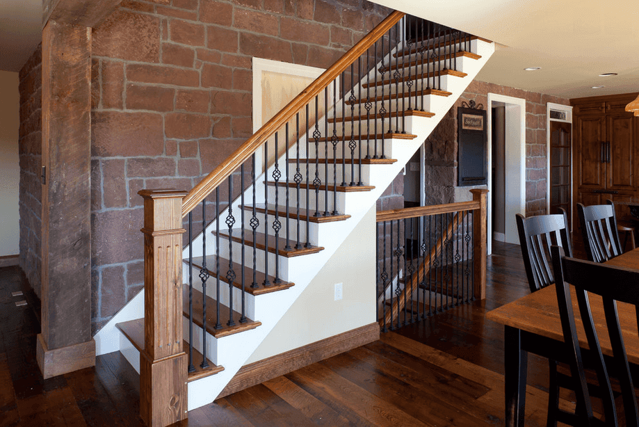 A bespoke wooden staircase pairs seamlessly with sleek black metal railings inside the home, nestled beside a striking stone wall and complemented by rich hardwood floors.
