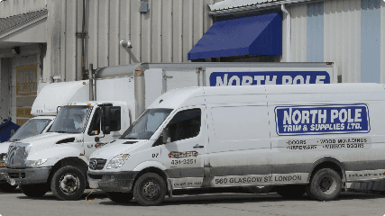 Three delivery trucks parked in front of a warehouse. The trucks display the branding for "North Pole Trim & Supplies Ltd.
