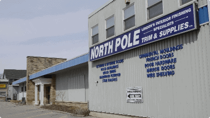 A commercial building with a sign reading "North Pole Trim & Supplies" offers various interior finishing products. The sign lists items such as moldings, doors, hardware, and shelving.